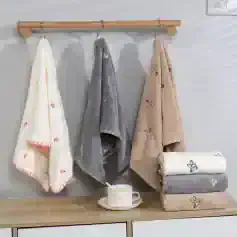 Soft plush towels with cute embroidery patterns hanging on a wooden rail in a modern bathroom decor, ideal for a cozy and stylish upgrade.