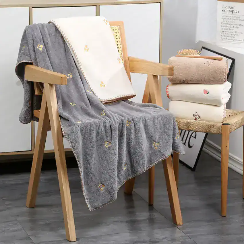 Luxurious embroidered towels and plush blankets displayed on wooden chairs at Monalisa Store, perfect for high-quality bathroom decor and gifting.