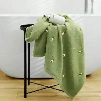 Luxurious green towel with embroidered smiley faces, placed over a black towel rack, next to a white skincare product in a modern spa setup. Perfect for skincare, wellness, and spa treatments.