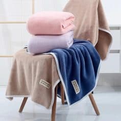 Luxurious plush towels in soft pink, lavender, and navy blue displayed on a modern chair for home or spa use, promoting comfort and relaxation.