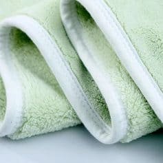 Fluffy green terry cloth towel with white trim, close-up detail, soft and plush fabric for skincare or spa use.