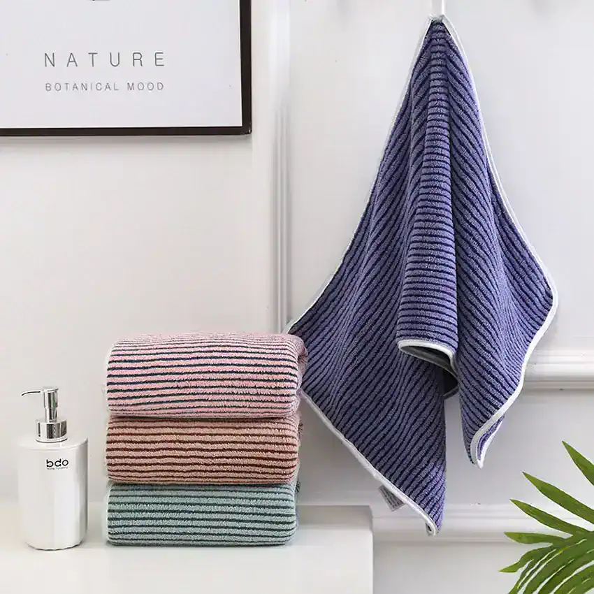 Fluffy striped towels and a hanging purple striped towel in a modern bathroom, featuring a soap dispenser and wall art, ideal for home decor and bathroom essentials.