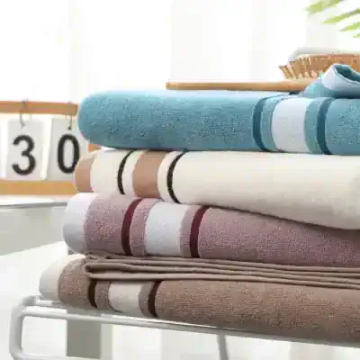 Soft, folded towels in pastel and neutral colors displayed on a white rack, representing high-quality textiles available at Monalisa Store for eye comfort and home relaxation.
