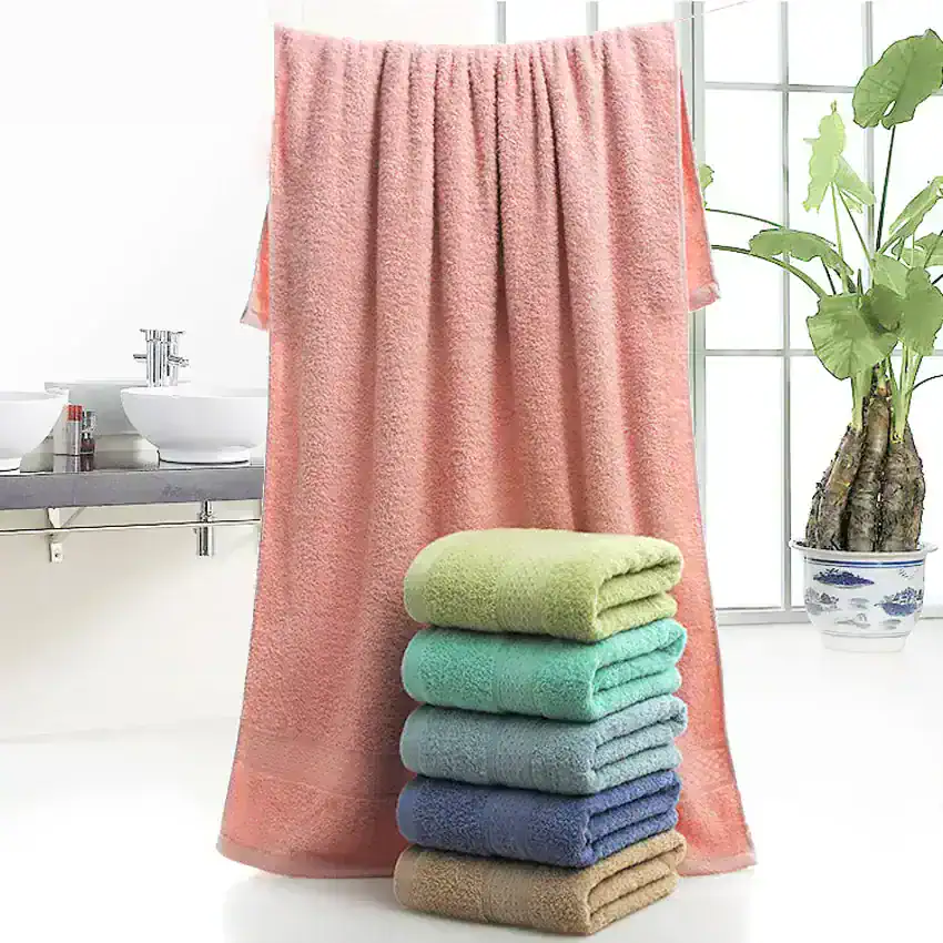Soft pastel-colored bath towels stacked in a bright, modern bathroom with large windows and a potted plant, emphasizing comfort and luxury in personal hygiene.
