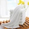 Soft white towels stacked on wooden slats with yellow tulips in the background, emphasizing luxurious towel offerings at Monalisa Store for skincare and home comfort.