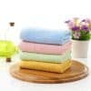 Soft pastel-colored towels stacked on a wooden tray with a potted purple flower and glass bottles in the background, perfect for spa, skincare, or beauty treatments at Monalisa Store.