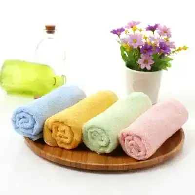Soft pastel-colored bath towels neatly rolled on a wooden tray with a flowerpot of colorful flowers and a bottle of bath oil in the background, emphasizing soothing spa and wellness products.