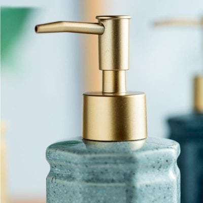 Sleek gold soap dispenser on textured blue ceramic container, modern bathroom decor for skincare and hygiene.