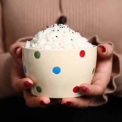 Creamy popcorn in a colorful polka dot bowl, held by a person with red nail polish; cozy indoor setting.