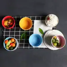 Colorful bowls and cups with fresh fruits and desserts on a black surface, showcasing modern tableware for healthy living and stylish kitchen accessories.
