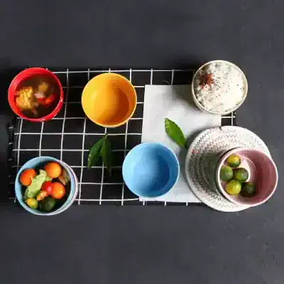 Colorful bowls and cups with fresh fruits and desserts on a black surface, showcasing modern tableware for healthy living and stylish kitchen accessories.