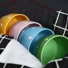 Multicolored ceramic bowls stacked in a wire basket for kitchen storage.