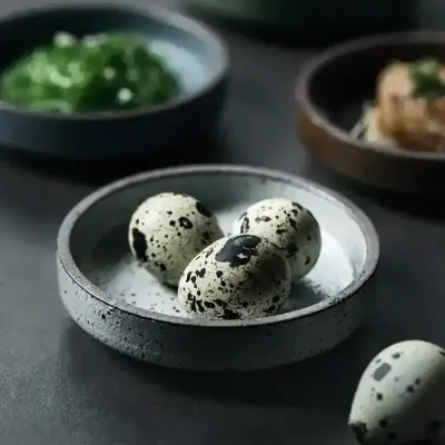 Whimsical speckled quail eggs in a black ceramic bowl, surrounded by green herbs and dishes, Mediterranean cuisine, high-quality food presentation, Monalisa Store, fresh ingredients, minimalistic aesthetic, culinary delicacies.
