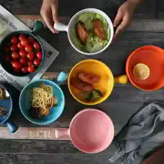Colorful coffee mugs with food on rustic wooden table, featuring cherry tomatoes, fried chicken, shrimp, lemon, and pasta - perfect for a casual meal or cafe setting.