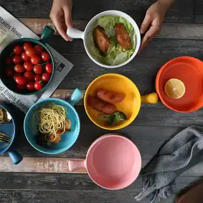 Colorful coffee mugs with food on rustic wooden table, featuring cherry tomatoes, fried chicken, shrimp, lemon, and pasta - perfect for a casual meal or cafe setting.