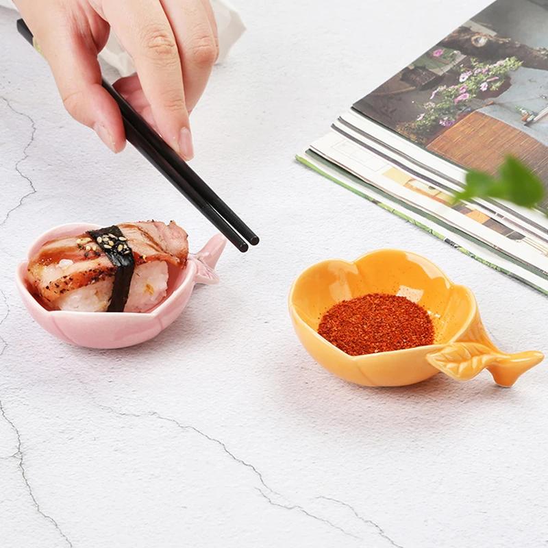Sushi in pink fish-shaped bowl with black chopsticks on a white textured surface, alongside a bowl of red chili powder, with magazines in the background, perfect for Japanese cuisine photography.