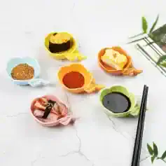 Colorful soy sauce and seasoning-filled sushi sauce dishes on a white textured surface with chopsticks and greenery.