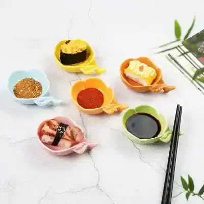 Colorful soy sauce and seasoning-filled sushi sauce dishes on a white textured surface with chopsticks and greenery.