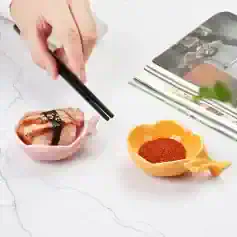 Sushi with chopsticks, spices in a yellow heart-shaped dish, pink ceramic plate with sushi, clean white background, Monalisa Store, sushi and spice essentials for Asian cuisine enthusiasts.