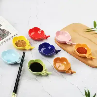 Colorful ceramic soy sauce dishes in various shades, perfect for sushi and Asian cuisine, displayed on a white surface with chopsticks and condiments.