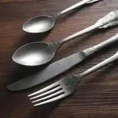 Elegant vintage silverware set including teaspoons, knife, and fork with ornate handles, displayed on wooden surface, perfect for dining and collection purposes.
