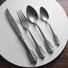 Shiny vintage silver cutlery set including knife, fork, and two spoons with ornate handles on a white textured plate, ideal for elegant dining.