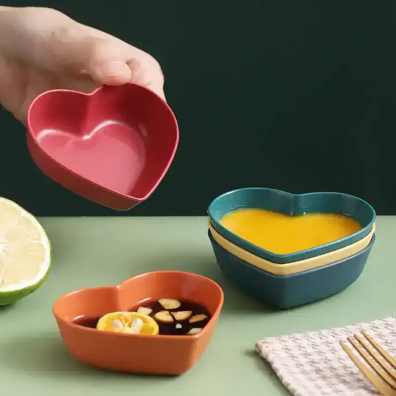 Heart-shaped ceramic bowls for dips and snacks, pink, blue, and orange, on a colorful table with lemon slices and soy sauce, perfect for serving food in style.