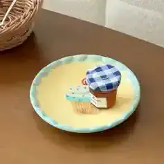 Miniature dessert jar with blue checkered lid, placed on a decorative pastel cupcake plate, on a wooden surface.