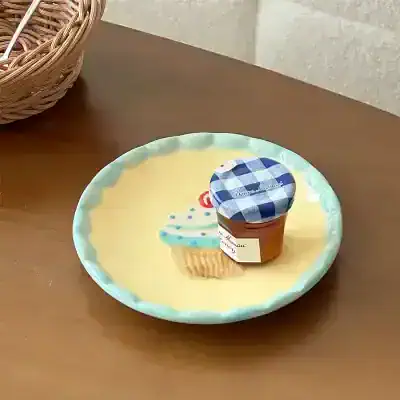 Miniature dessert jar with blue checkered lid, placed on a decorative pastel cupcake plate, on a wooden surface.