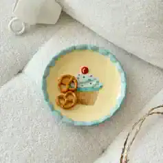 Cupcake birthday cake with pretzel decorations and birthday candle on a decorative plate.