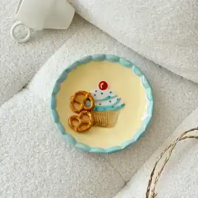 Cupcake birthday cake with pretzel decorations and birthday candle on a decorative plate.