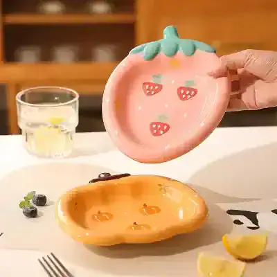 Pink strawberry-shaped ceramic dish with green leaf detail, ideal for kitchen decor or serving small snacks.
