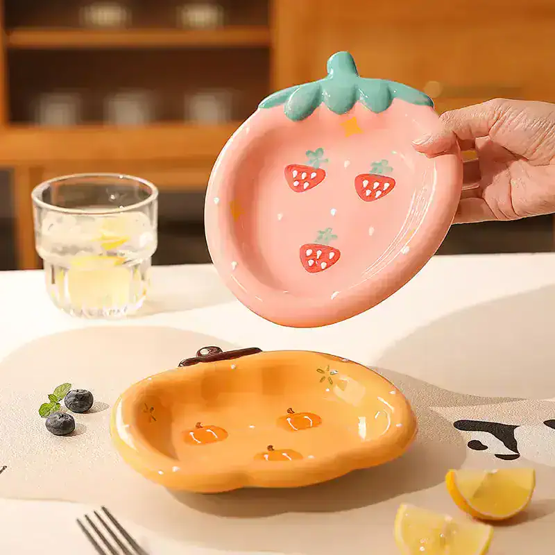 Pink strawberry-shaped ceramic dish with green leaf detail, ideal for kitchen decor or serving small snacks.