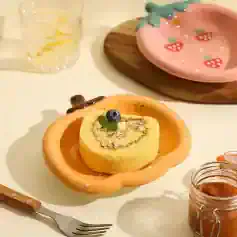 Vanilla sponge cake roll with cream filling topped with a blueberry and mint leaf, served on a peach-colored ceramic plate with a strawberry design, perfect for a sweet treat at Monalisa Store.