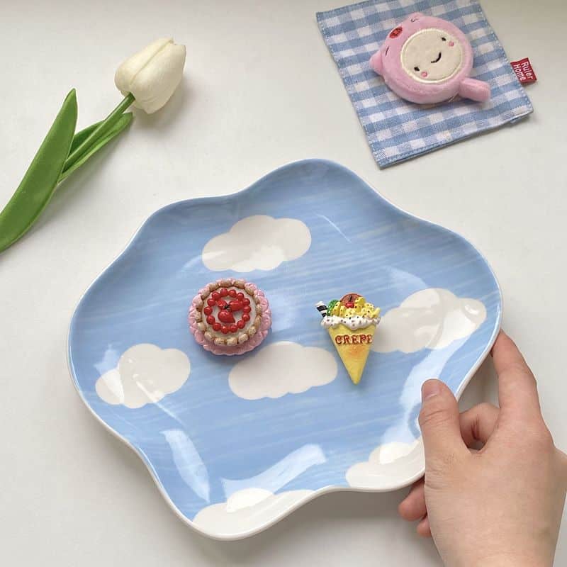 Delicate pink and white character-themed plush toy on blue checkered cloth, smiling face, adorable children's accessory, cute and soft plush, perfect for babies and young kids.