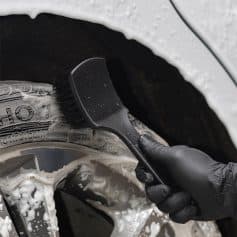 Car wheel cleaning brush for automotive detailing and maintenance, black handle and bristles, being used on a tire with soap suds, in a car wash or detailing context, high quality vehicle care product.