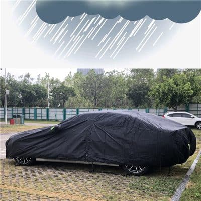 Uncovered car parked outdoors under a dark cloud with rain, covered by a black protective car cover, in a parking lot with trees and a fence in the background, showcasing vehicle protection and car accessories.