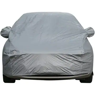 Gray car covered with protective plastic car cover for outdoor storage.