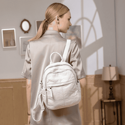 Elegant woman carrying a white leather backpack, wearing a light gray satin blazer, in a modern art gallery setting, showcasing stylish accessories for women or students.