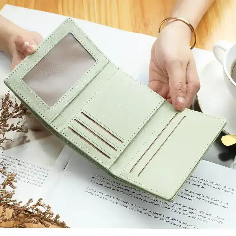 Wallet with multiple card slots and a transparent ID window, in soft pastel color, on a wooden table with a cup of coffee.