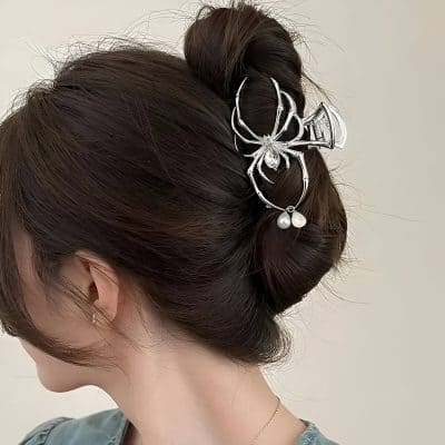 Elegant woman with expertly styled dark brown hair in a neat bun, adorned with a silver insect-shaped hair accessory featuring pearl accents; perfect for sophisticated or special occasions.