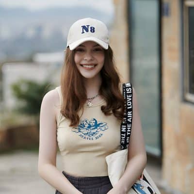 N8 white baseball cap, smiling young woman outdoors, casual fashion with tank top, hairstyle, and accessories, lifestyle shot for Monalisa Store.