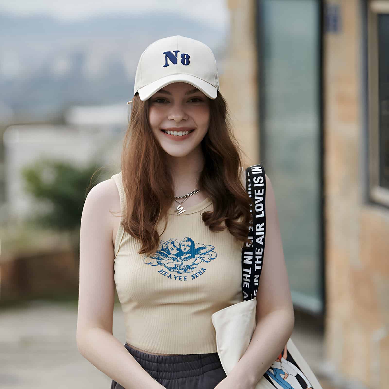N8 white baseball cap, smiling young woman outdoors, casual fashion with tank top, hairstyle, and accessories, lifestyle shot for Monalisa Store.