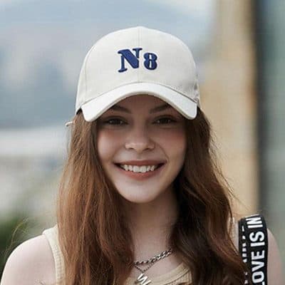 Cute woman wearing a white baseball cap with "N8" and casual fashion, smiling outdoors.