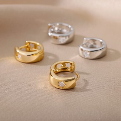 Shiny gold and silver hoop earrings with star-shaped diamonds on a beige satin surface.