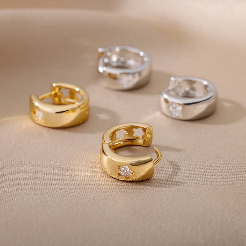 Shiny gold and silver hoop earrings with star-shaped diamonds on a beige satin surface.