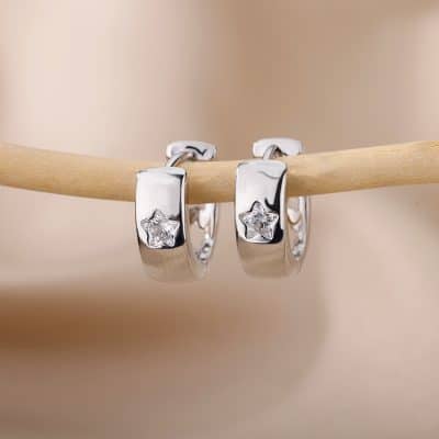 Shiny silver hoop earrings with star-shaped gemstones hanging on a wooden stick, perfect for stylish women.