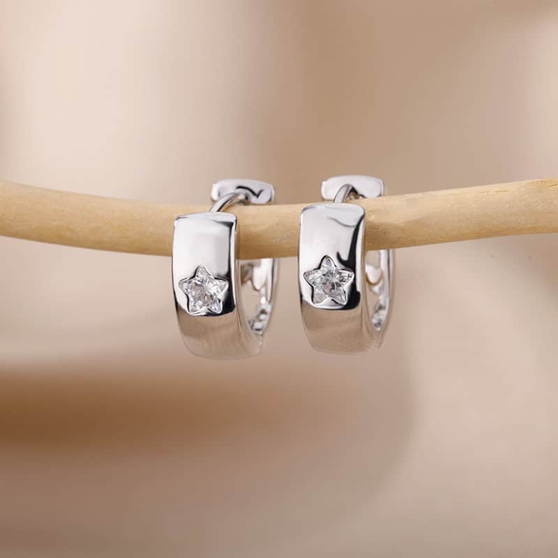 Shiny silver hoop earrings with star-shaped gemstones hanging on a wooden stick, perfect for stylish women.