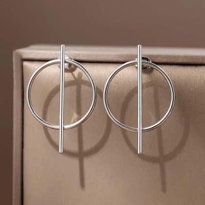 Shiny silver hoop and bar earrings displayed on beige jewelry box, modern minimalist jewelry design for women.