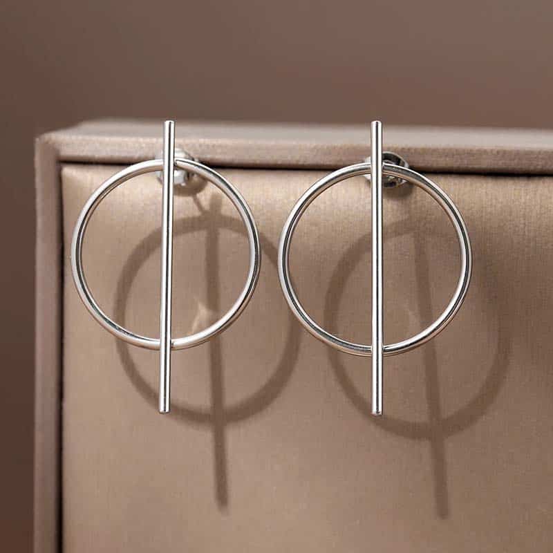 Shiny silver hoop and bar earrings displayed on beige jewelry box, modern minimalist jewelry design for women.
